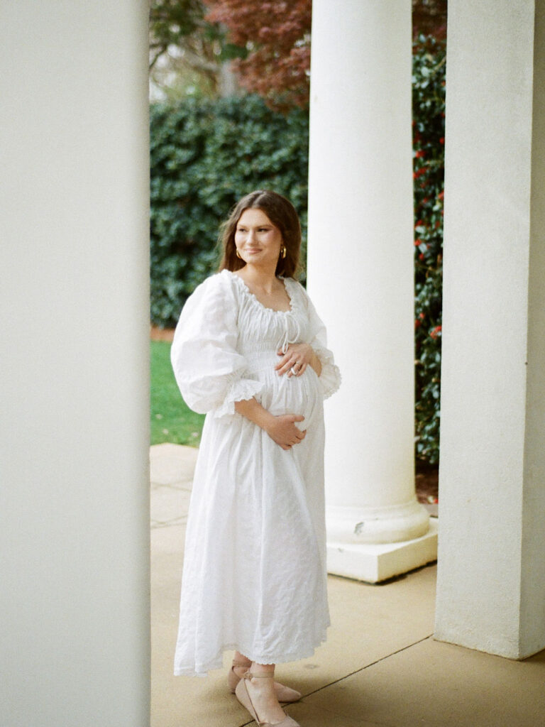 A pregnant woman in a white dress walks through the Huntsville Botanical Garden at her North Alabama maternity photo session.