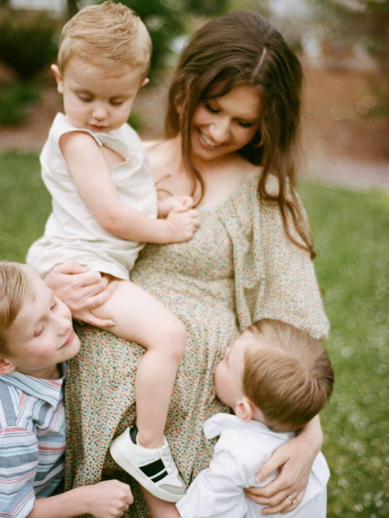 A sweet moment between a mother and her three young sons, with two hugging her while she holds the youngest, during her Huntsville Botanical Garden maternity photo session.
