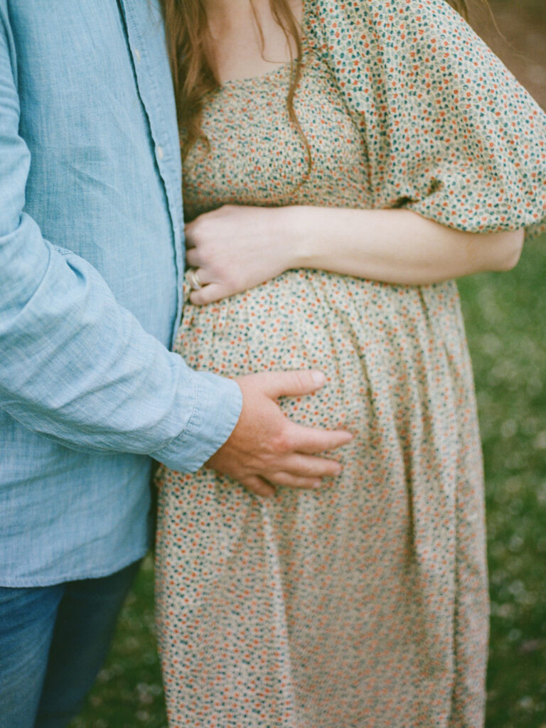 A man gently rests his hand on his wife's pregnant belly during their Huntsville Botanical Garden maternity photo session on film.