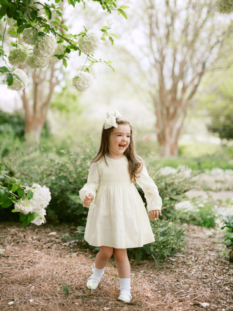 A little girl in a yellow dress laughs during family photos at the Huntsville Botanical Garden,