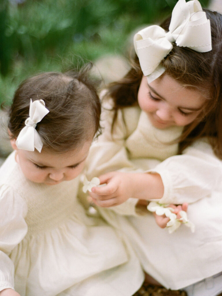 Two toddlers in yellow dresses with bows in their hair pose together during their Huntsville Botanical Garden family photos.