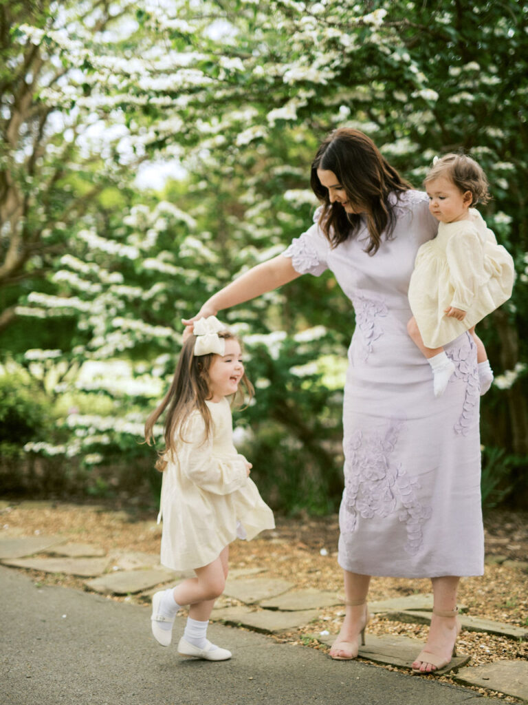 A mother holds her toddler on one hip while her other daughter does a twirl at the Huntsville Botanical Garden