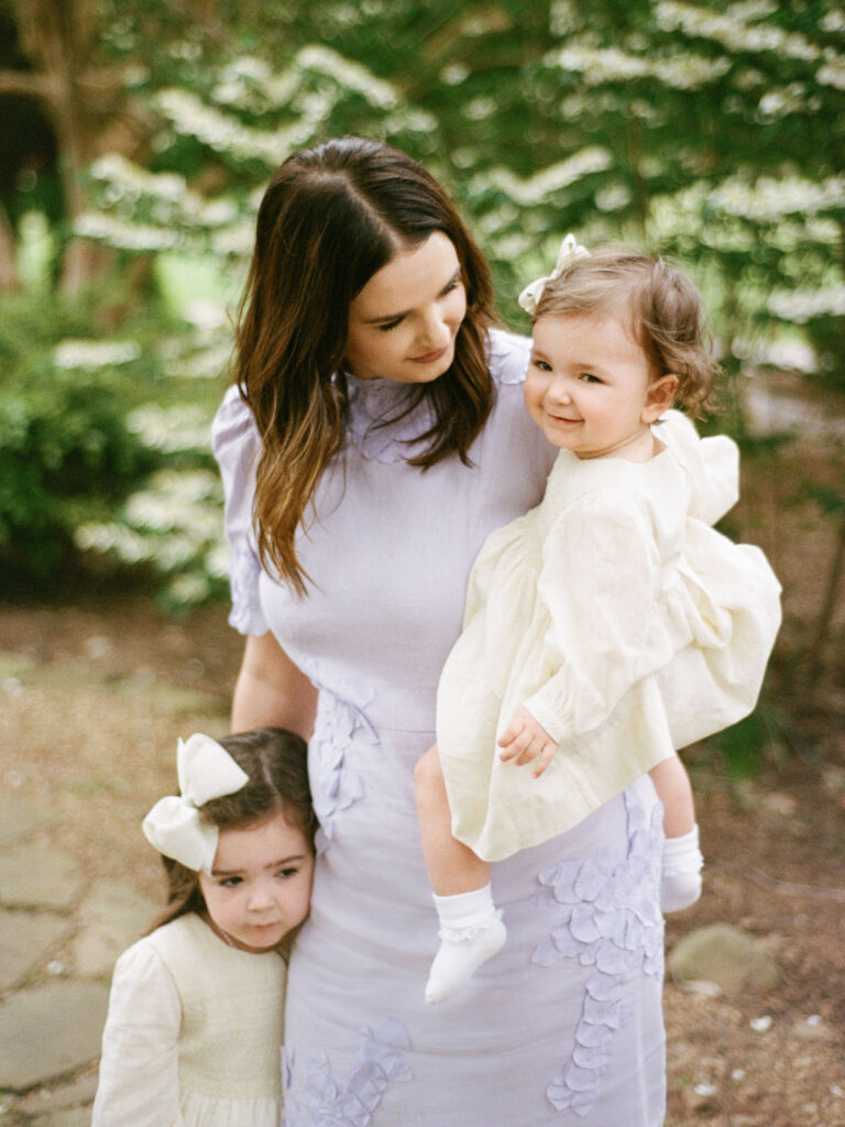 A mother poses at the Huntsville Botanical Garden with her two young daughters, one held on her hip and the other standing next to them