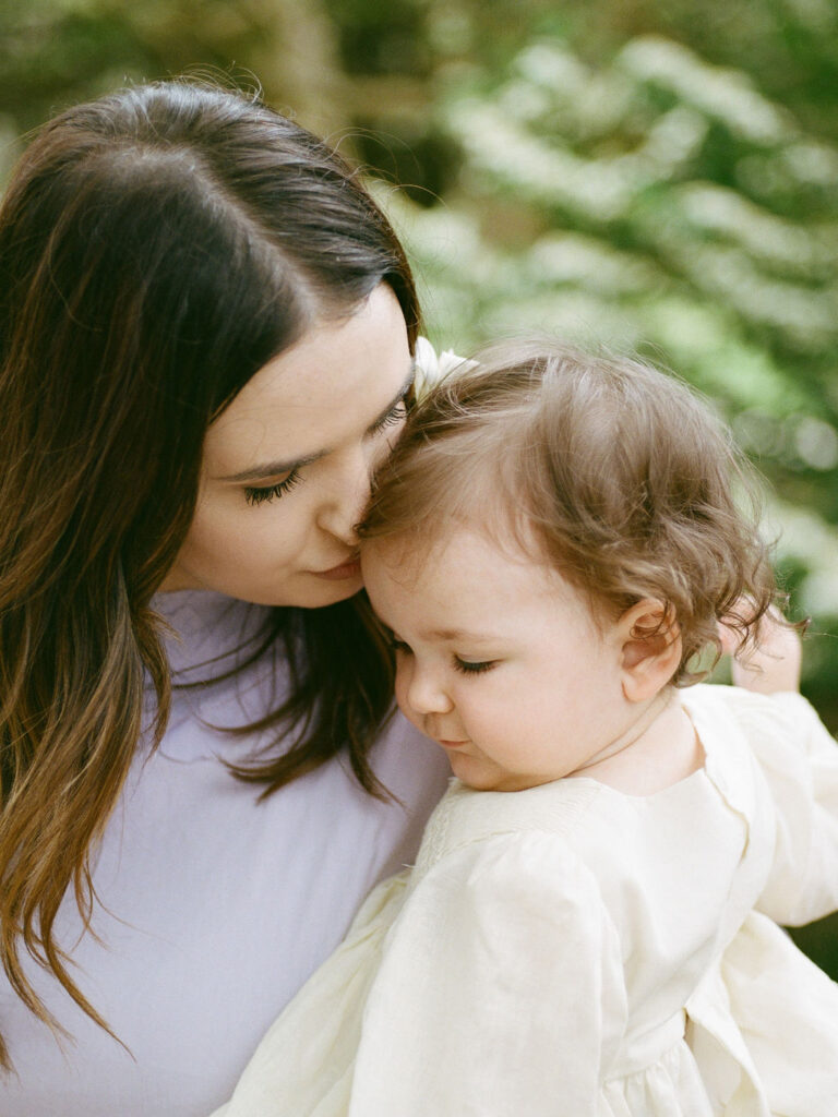 A mother in a purple dress kisses her toddler daughter's forehead during their Huntsville Botanical Garden family photoshoot