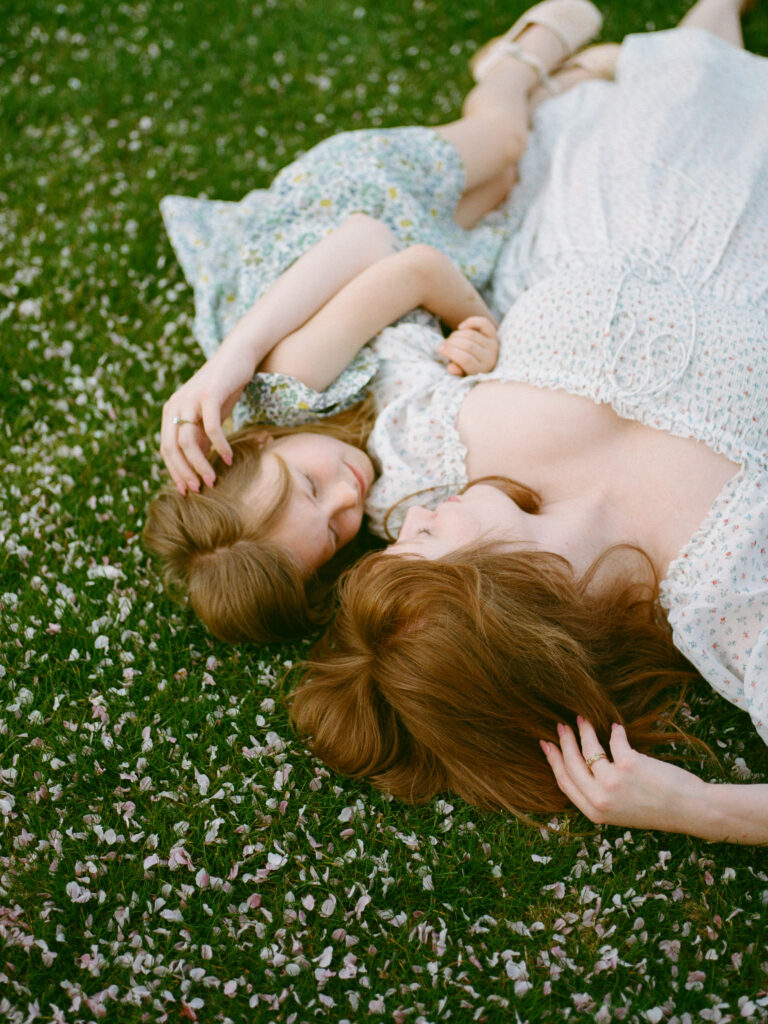 A mother and her daughter lying in a lush field with pink petals at the Huntsville Botanical Garden