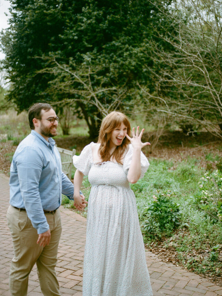 A couple laughing as the woman shows off her ring for the camera at their Huntsville Botanical Garden proposal
