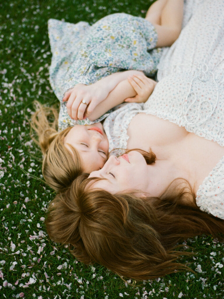 A mother and her daughter lying in a lush field with pink petals at the Huntsville Botanical Garden