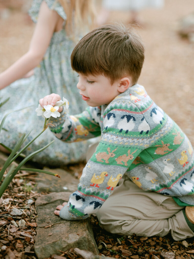 A young boy sits on the ground at the Huntsville Botanical Garden and smells a daffodil 