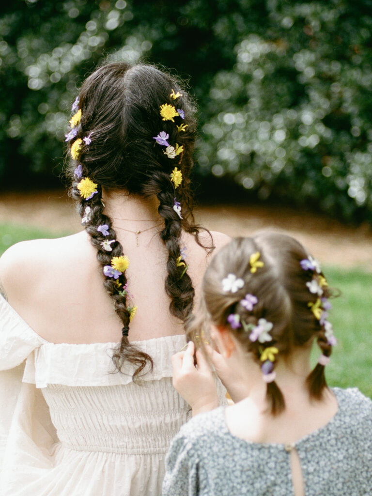 A small child puts flowers in her mother's braided hair at their Huntsville motherhood photography session with Fauna & Film