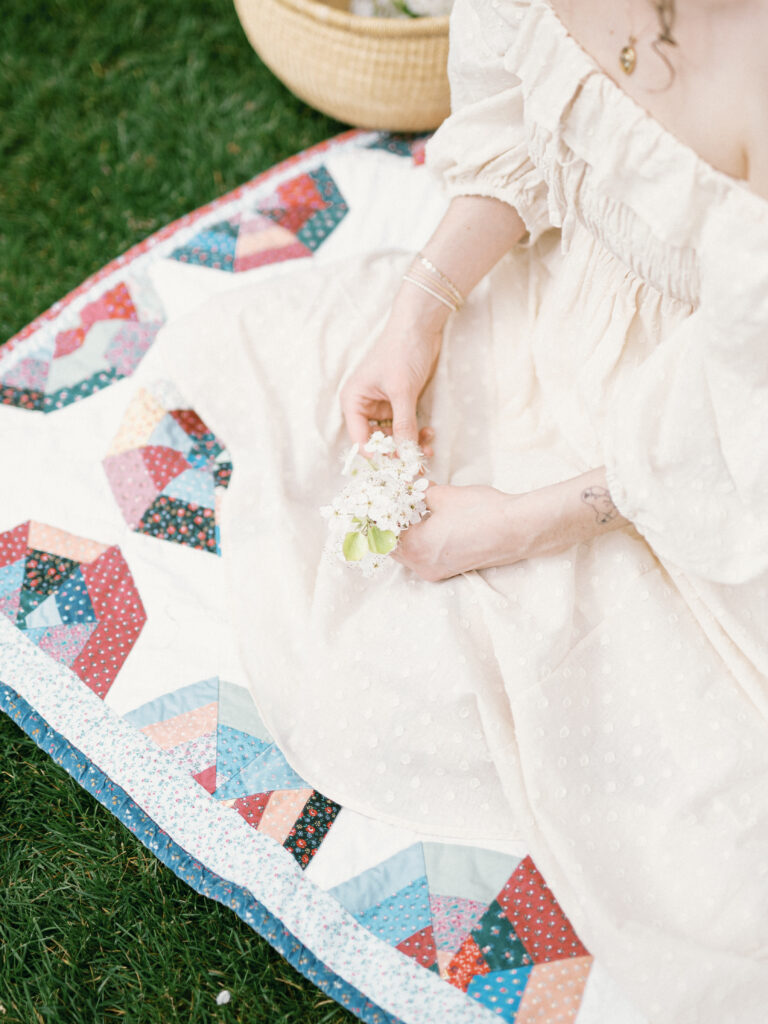 A woman sits on a picnic blanket holding a hydrangea flower