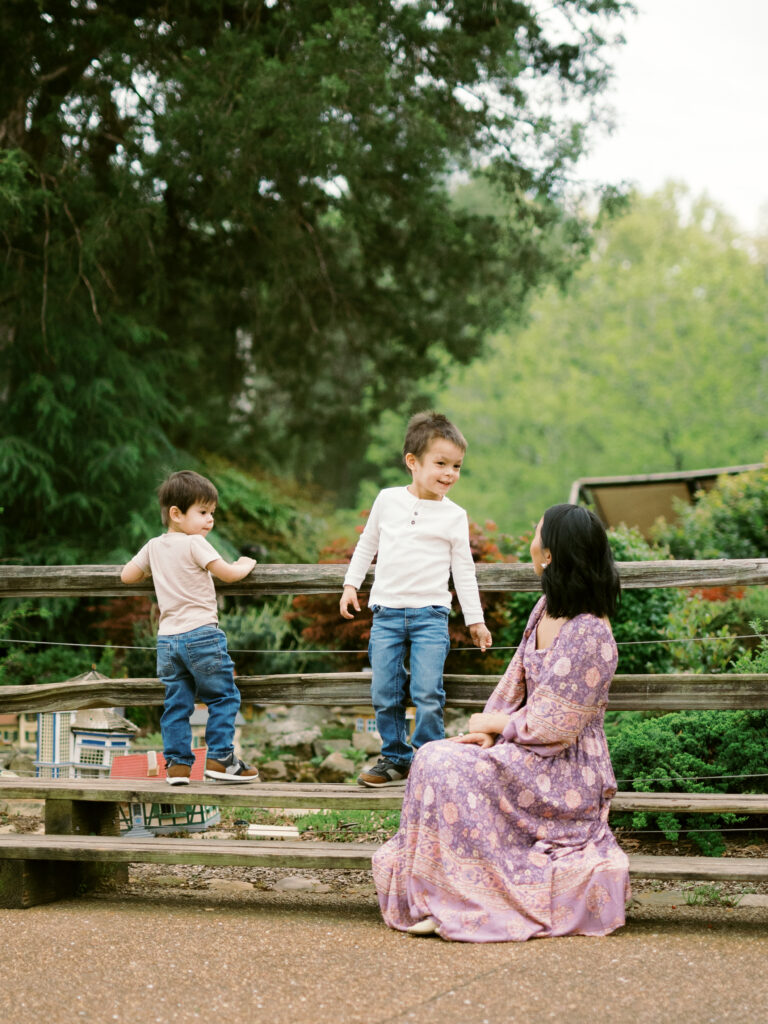 A woman sits on a bench looking at her two young children during their family photos at the Huntsville Botanical Garden.