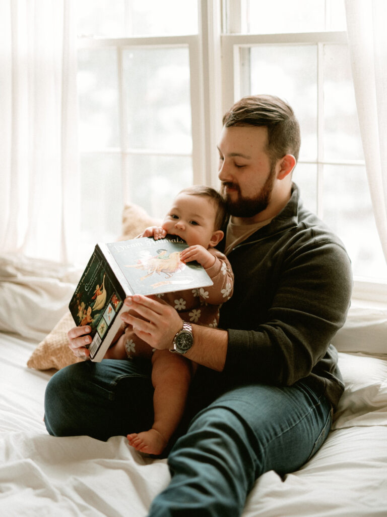 A man reads a book to his baby in bed at their family photos at home