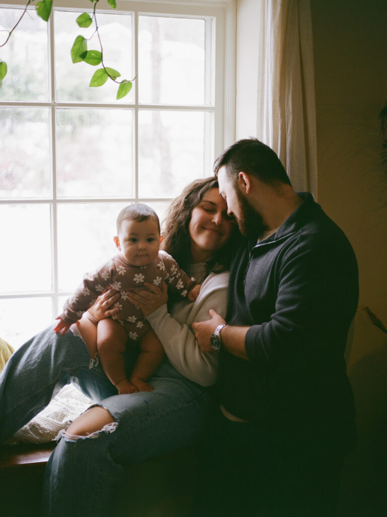 A family poses together by a window during their family photos at home