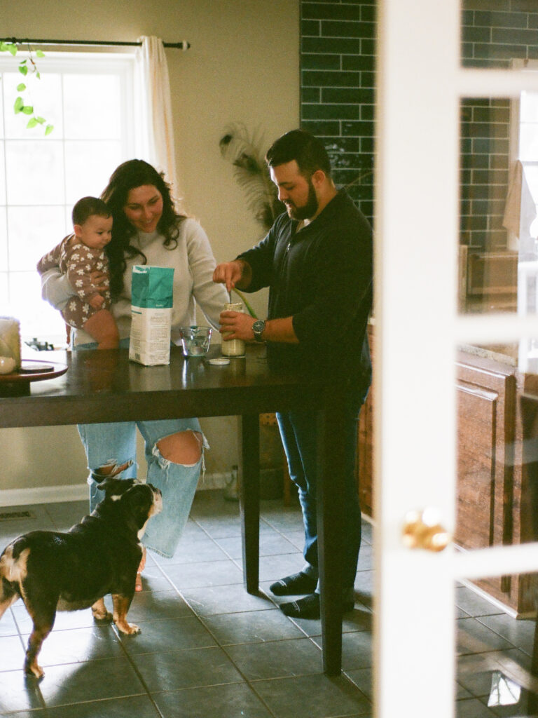 A man and a woman bake together at their kitchen table with their baby