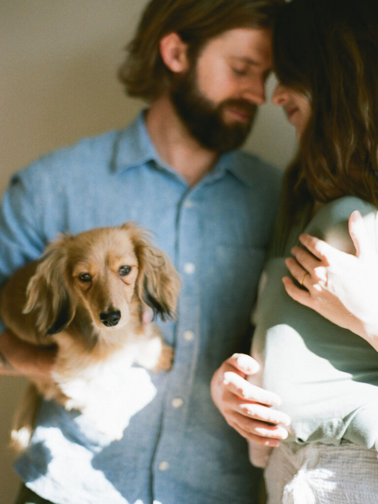 a couple poses with their newborn baby and dachshund