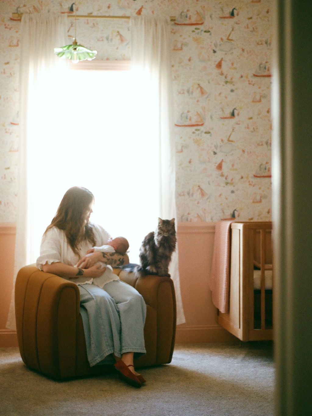 mother in modern nursery chair holding newborn while cat perches on armrest