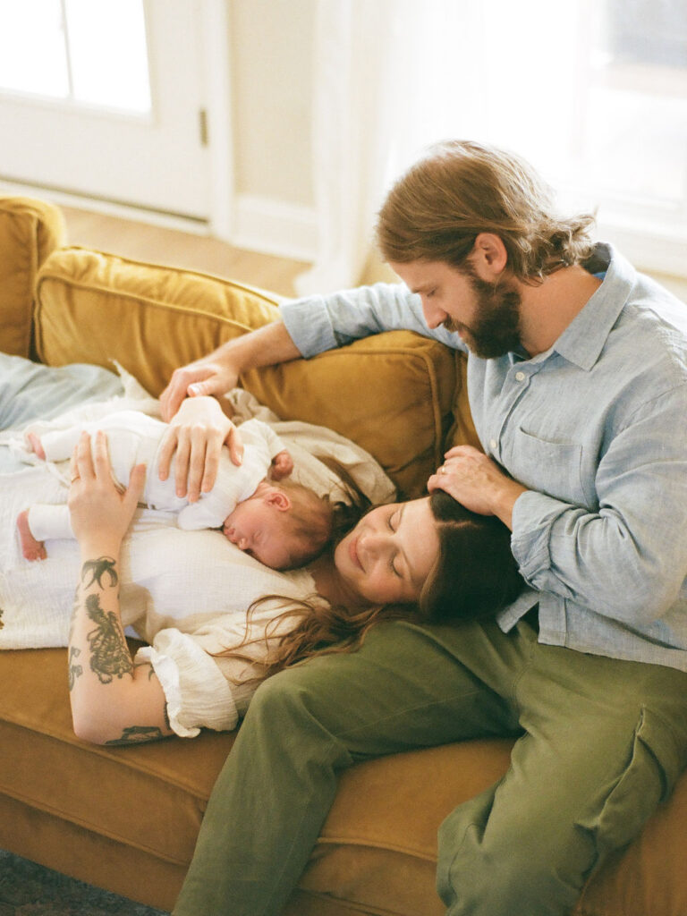 a family lounges together on a couch during their newborn photos at home